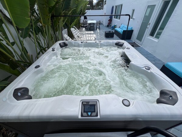A hot tub with a control panel, surrounded by outdoor furniture and plants.