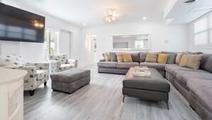 A modern living room with a grey sectional sofa, matching armchairs, and a flat-screen TV mounted on the wall. - 4/5 for 8, Steps to Beach-Jacuzzi, Furnished Patio (Hollywood)