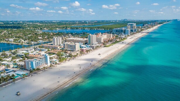 An aerial view of a coastal city with a long sandy beach, clear blue waters, and a mix of high-rise and low-rise buildings along the shoreline. - 4/5 for 8, Steps to Beach-Jacuzzi, Furnished Patio (Hollywood)