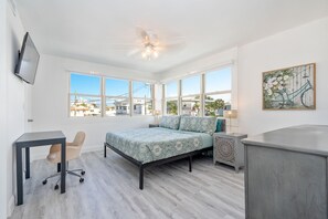 A bedroom with a bed, a desk, a chair, a TV, and a painting.