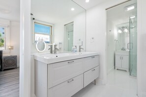 A modern bathroom with a large mirror, dual sinks, and a glass-enclosed shower.
