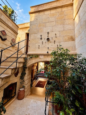 A stone building with a staircase leading to an upper level, a wall with hanging keys, and a courtyard with plants. - Shadow Cave House (Ürgüp)