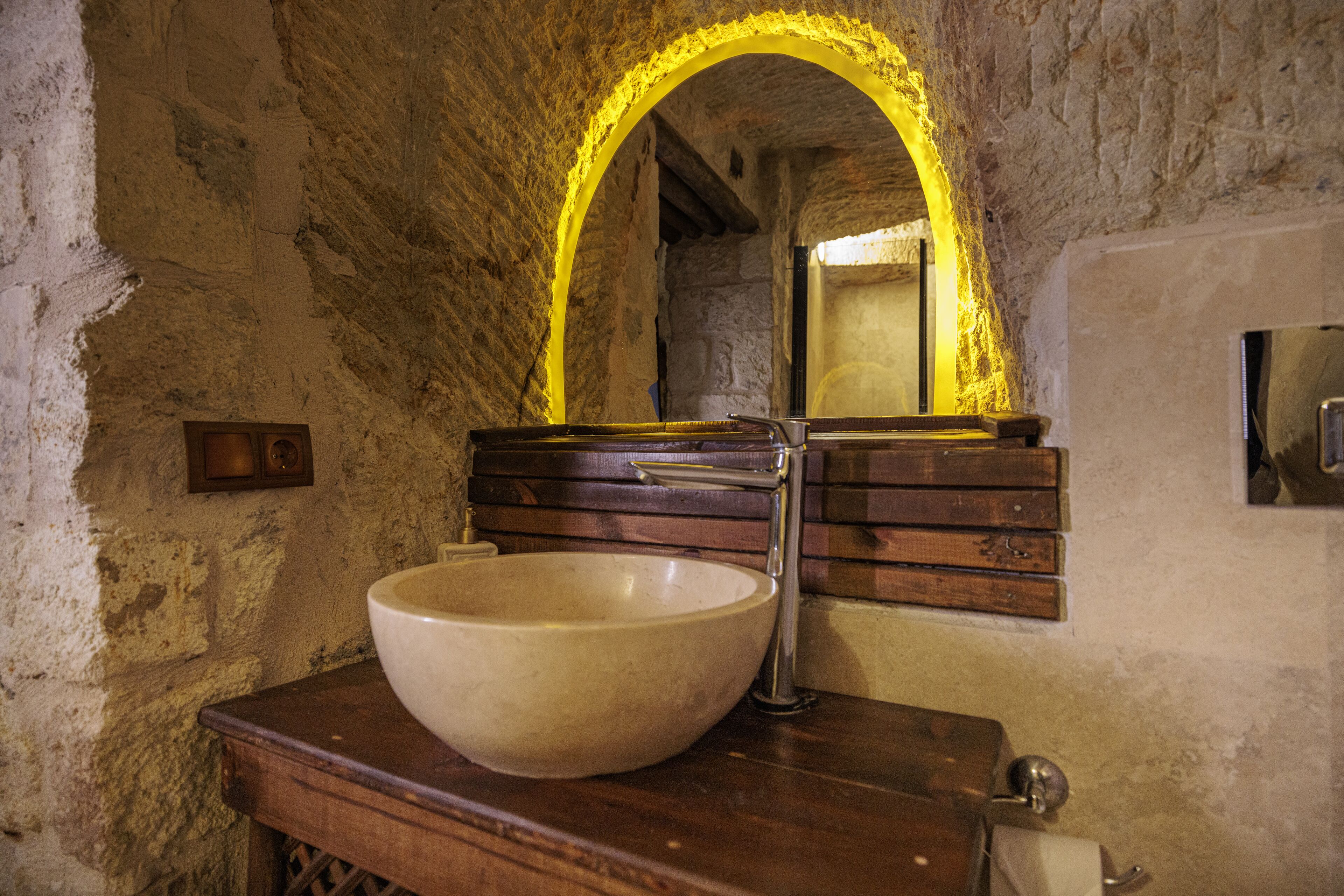 Un baño rústico con un lavabo grande tipo cuenco, tocador de madera y un espejo con arco amarillo.