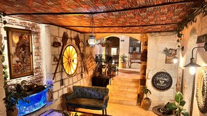A cozy room with a brick wall, a large wooden ceiling, a blue sofa, a wooden coffee table, and a fish tank. - Shadow Cave House (Ürgüp)