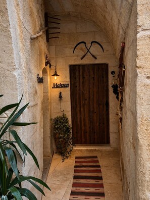 A narrow hallway with a wooden door, a potted plant, and a striped rug on the floor. - Shadow Cave House (Ürgüp)