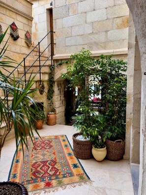 A courtyard with a stone wall, a staircase, potted plants, and a colorful rug. - Shadow Cave House (Ürgüp)