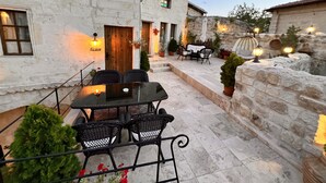 An outdoor patio with stone walls, a table with chairs, and potted plants. - Shadow Cave House (Ürgüp)