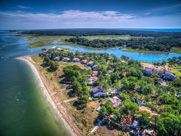 An aerial view of a coastal residential area with houses, a beach, and a lake.