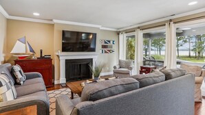 A living room with a fireplace, a large TV, and a view of the outdoors. - Enjoy Views of Calibogue Sound from Private Deck! (Hilton Head Island)