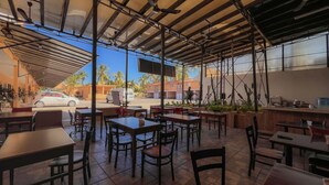 An outdoor cafe with tables and chairs, a covered seating area, and a view of palm trees and buildings in the background. - Hotel Oasis (Mazatlán)