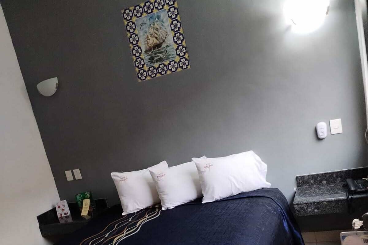 A bedroom with a bed, pillows, a bedside table, a wall clock, and a framed picture.