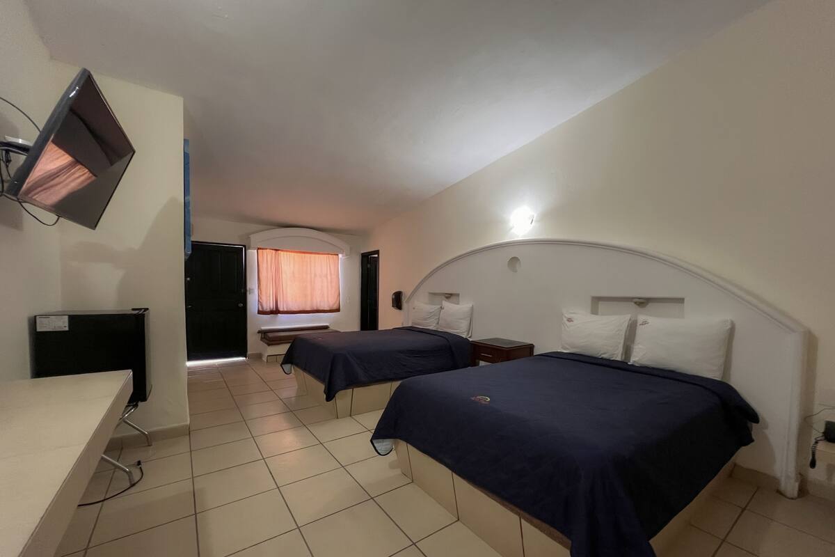 A hotel room with two beds, a desk, a television, and a window with curtains.