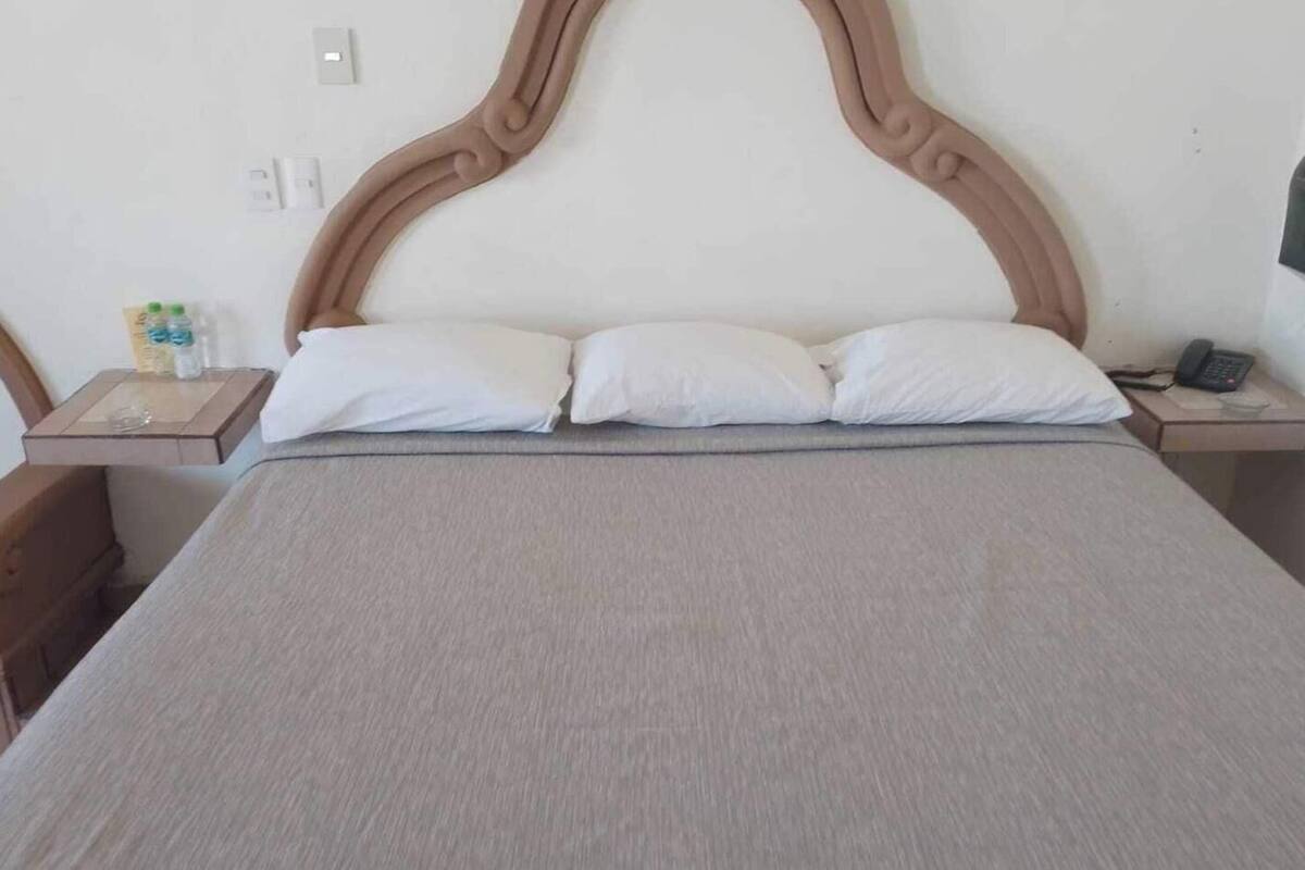 A bed with a headboard, two pillows, a bedside table with a phone, and a wall-mounted light.