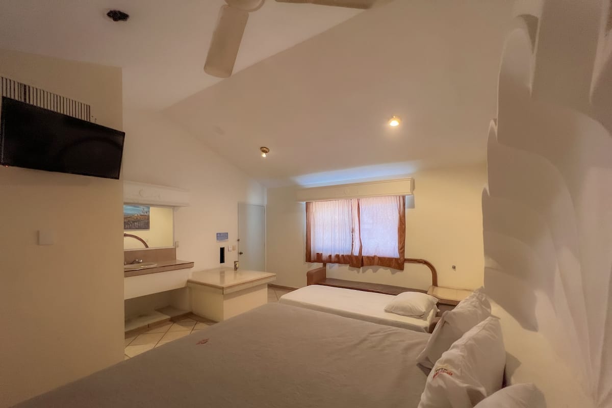 A hotel room with a bed, a bedside table, a mirror, a window with curtains, and a television mounted on the wall.