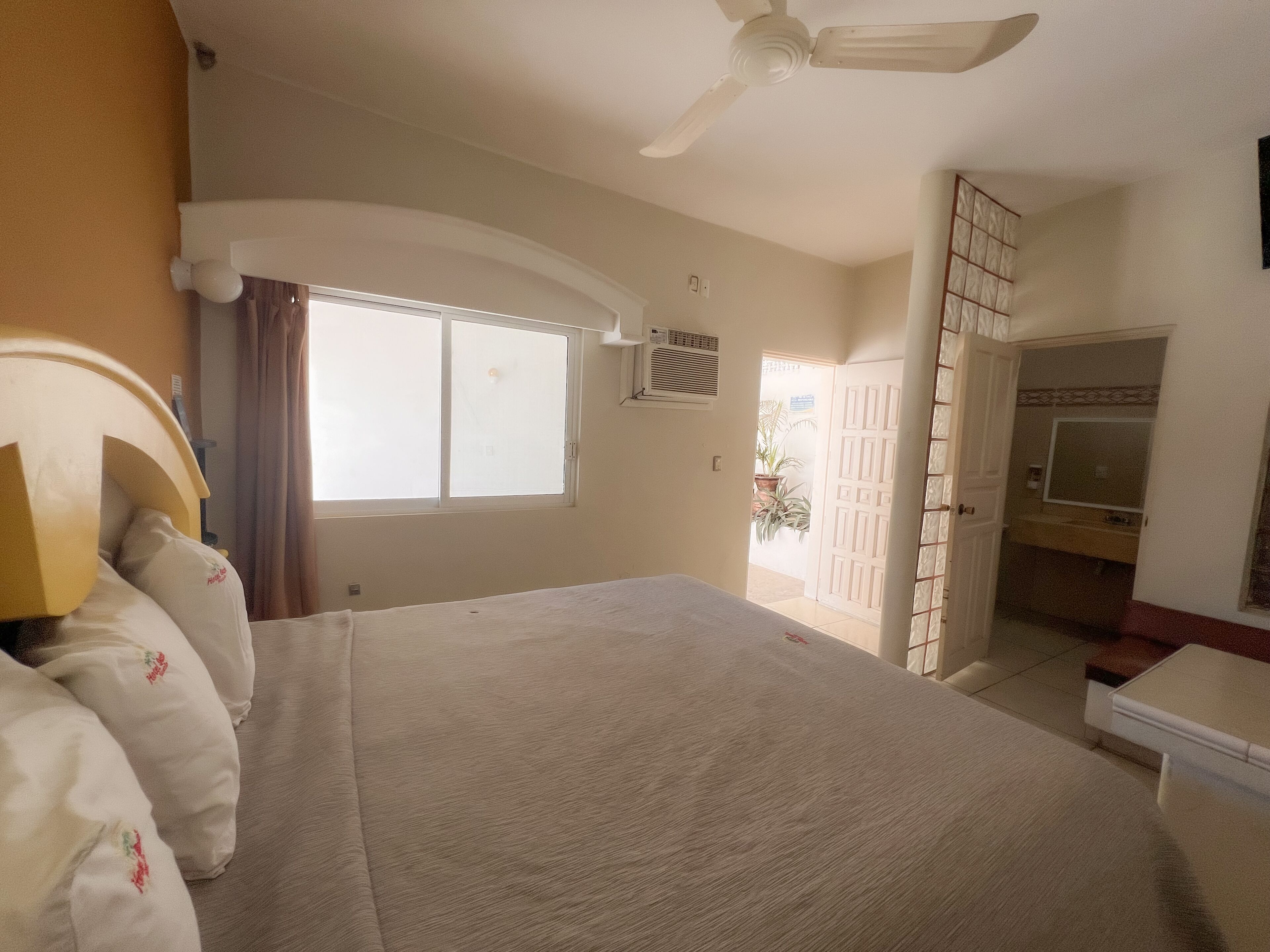 A bedroom with a bed, a ceiling fan, a window, and a door leading to a bathroom.
