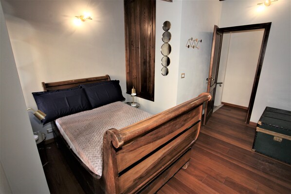 A bedroom with a wooden bed, a bedside table, a lamp, a mirror, and a wardrobe.