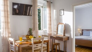 Una habitación con una mesa de comedor de madera, sillas, un taburete pequeño, un espejo, una cama y un televisor montado en la pared.