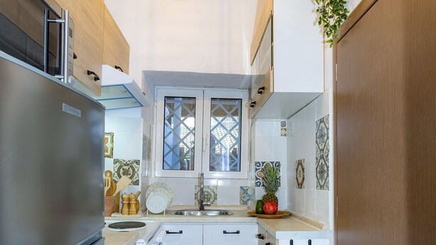 Una cocina compacta con armarios blancos, un refrigerador de acero inoxidable, una lámpara colgante y una ventana pequeña.