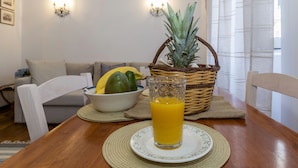 Una mesa de comedor con un vaso de jugo de naranja, un plato y una cesta de mimbre con frutas.