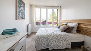 A bedroom with a bed, a bedside table, a window with curtains, and a painting on the wall.