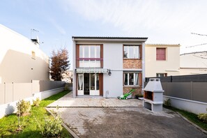 A two-story house with a paved driveway, a lawn, and a barbecue grill.