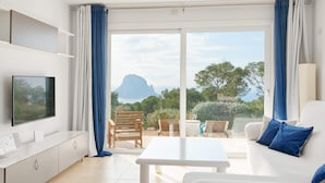 Un salon moderne doté d’un téléviseur à écran plat, d’un canapé, d’une table basse et d’un balcon offrant une vue sur une montagne et la verdure.
