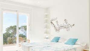 Une chambre avec deux lits, une porte-fenêtre coulissante donnant sur un balcon et un motif décoratif représentant une branche d’arbre sur un des murs.
