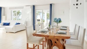 Un espace repas moderne avec une table en bois, des chaises blanches et une vue sur l’extérieur.