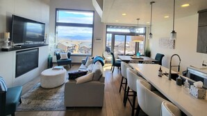 Un espacio moderno y abierto que integra sala y comedor, con un amplio ventanal, televisor de pantalla plana y cocina con barra.