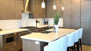 Una cocina moderna con armarios de madera, una isla central con taburetes y un horno empotrado, además de iluminación colgante.