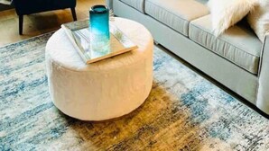 Una sala moderna con un sofá gris, un reposapiés redondo y una mesa de centro de vidrio.