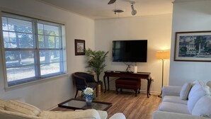 Ein Wohnzimmer mit einer Couch, einem Couchtisch, einem Fernseher, einer Lampe und einem Gemälde an der Wand.