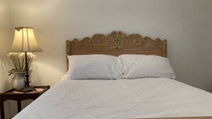 Ein ordentlich bezogenes Bett mit Holzabdeckung, eine Nachttischlampe mit Blumenvase und ein kleiner Nachttisch aus Holz.