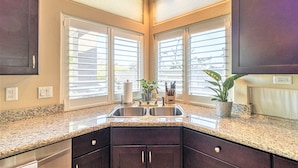 A kitchen with granite countertops, dark cabinets, a double sink, and large windows with blinds. - Gardenesque oasis getaway w/cooling water misters (Phoenix)