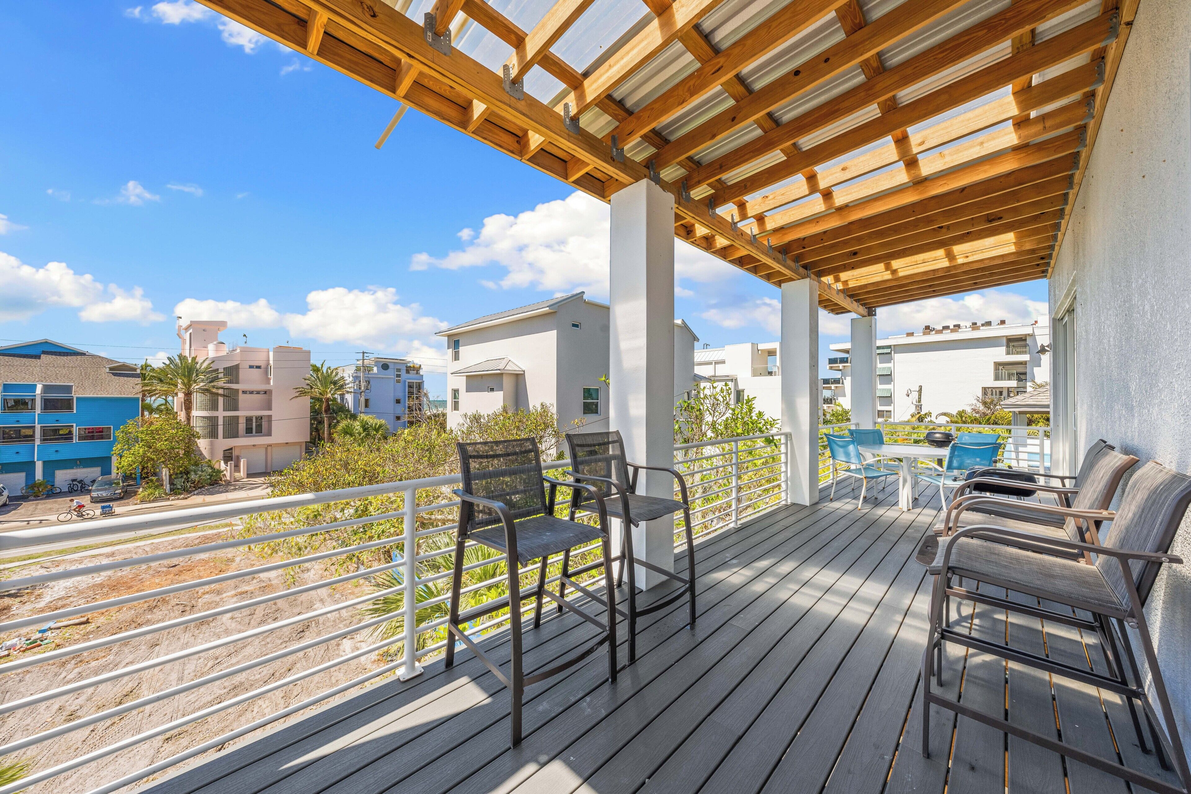 A covered outdoor area with wooden flooring, metal chairs, and a white railing.