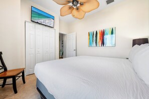 Un dormitorio con una cama grande, un ventilador de techo, un televisor en la pared y un cuadro abstracto colorido.