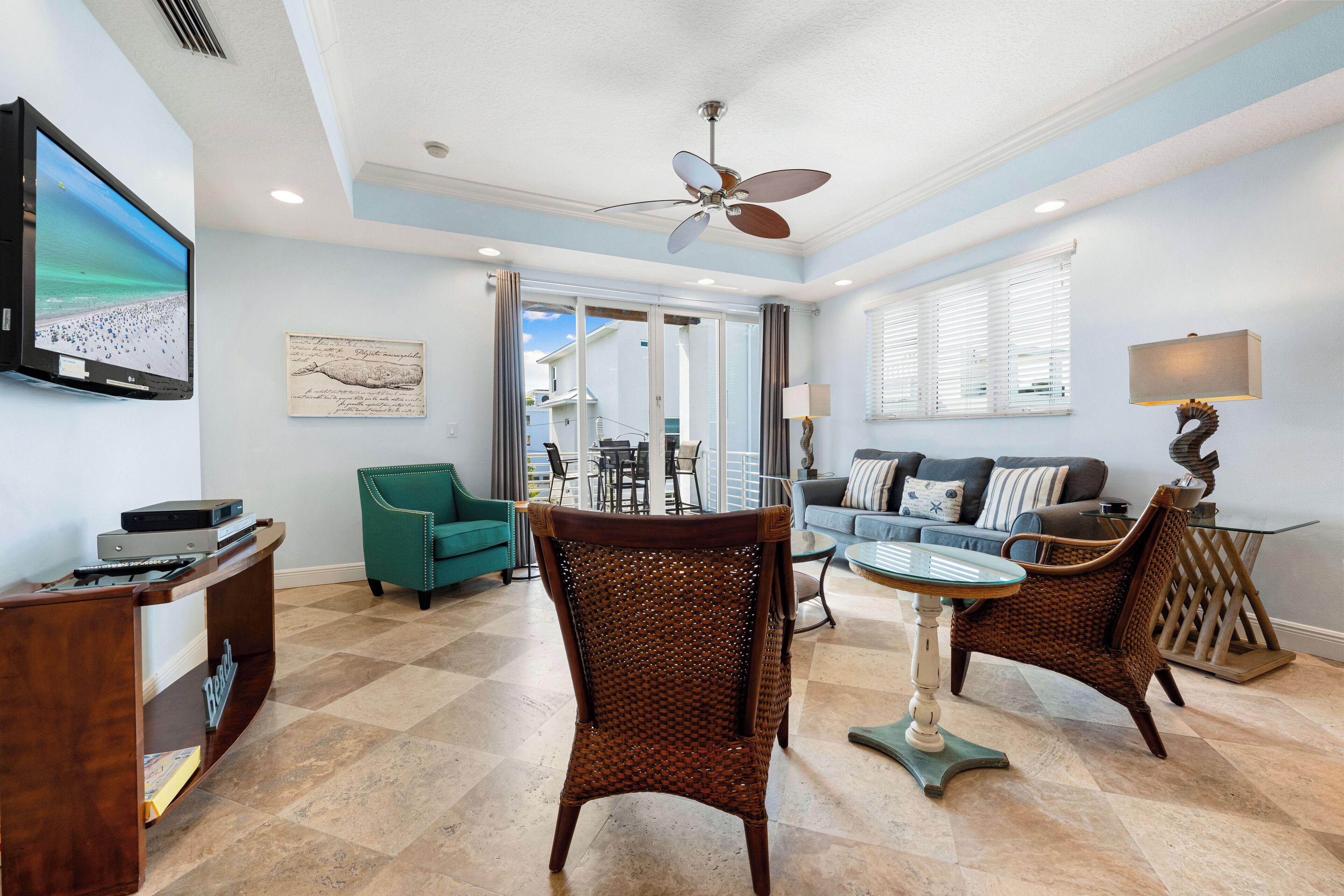 A spacious living room with a large flat-screen TV, a ceiling fan, and a dining area with a glass table and chairs.