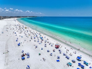 Une vaste plage parsemée de nombreux parasols et de chaises longues, une tour de surveillance pour les sauveteurs et une vue dégagée sur l’océan.