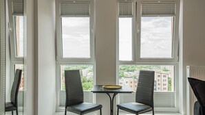 Habitació amb dues cadires i una taula a prop d'una finestra amb persianes, amb vista a un paisatge urbà.