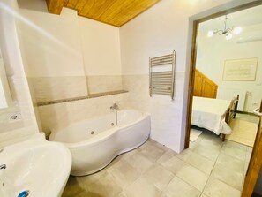 A bathroom with a bathtub, a sink, and a shower. There is a towel rack on the wall and a wooden ceiling.