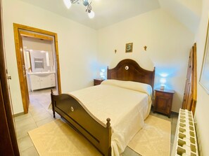 A bedroom with a wooden bed, bedside lamps, a mirror, and a bathroom visible through an open door.