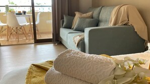 A living room with a sofa, a yellow rug, and a small table with chairs. - Apartment in complex with heated pool. (Los Cristianos)