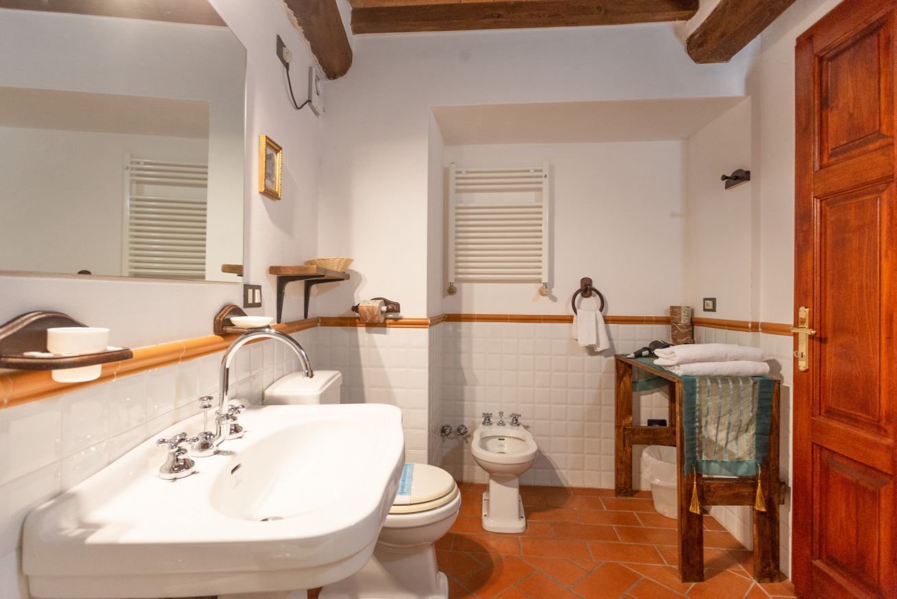 A bathroom with a sink, toilet, bidet, and wooden bench.