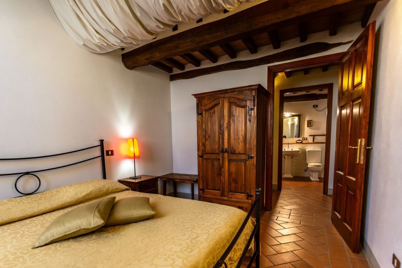 Ein Schlafzimmer mit einem Bett, einem Holzschrank, einem Nachttisch und einem durch eine offene Tür erreichbaren Badezimmer.