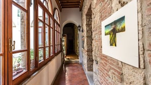 Un pasillo con ventanas de madera, un muro de ladrillo con un cuadro enmarcado y piso de baldosas.