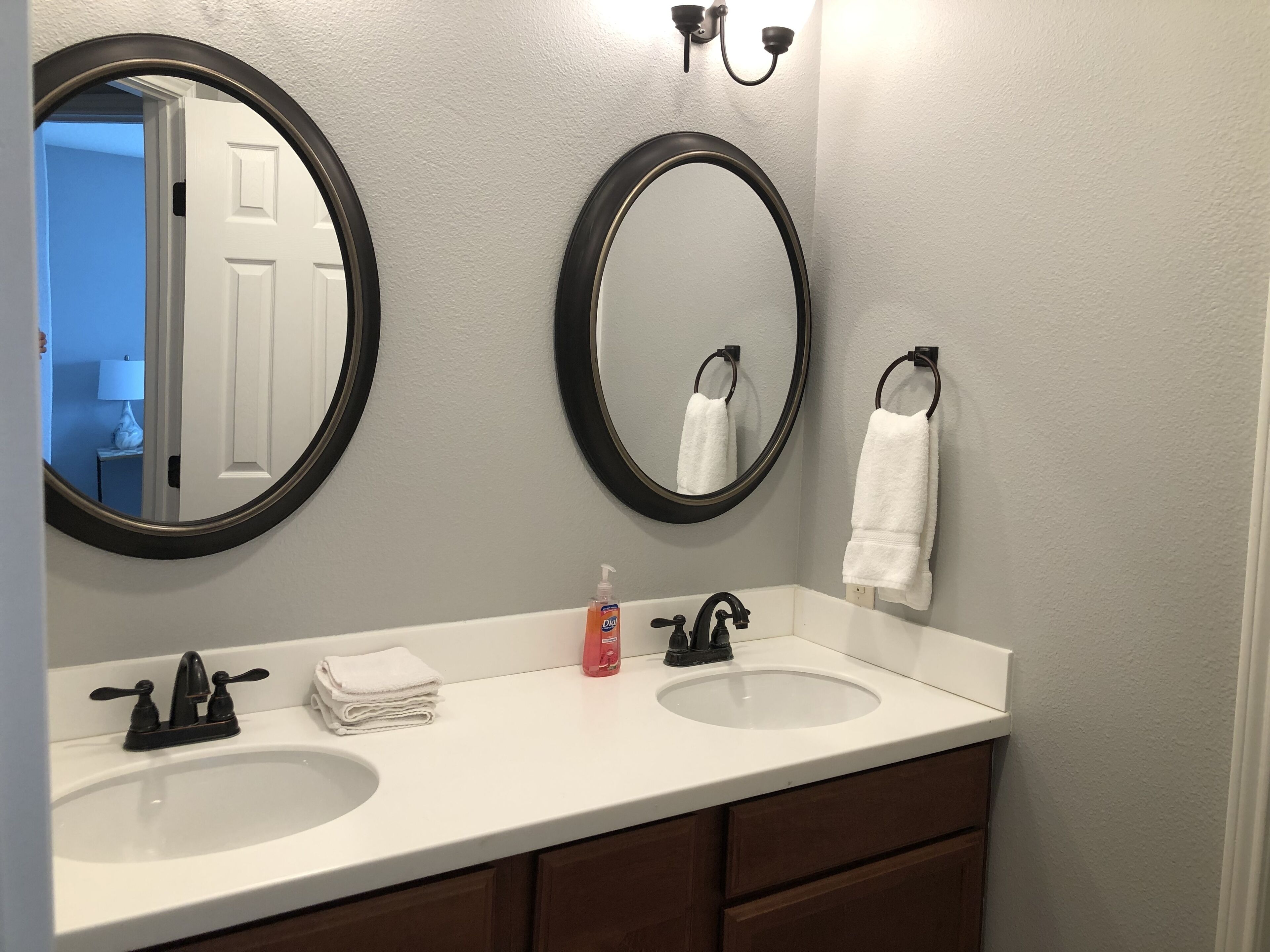 A bathroom with two sinks, a mirror, a towel rack, and a bottle of hand soap.
