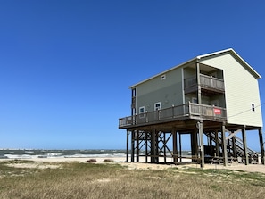 A two-story beach house with a balcony on the upper floor, situated on stilts over the sand. - Escape at Treasure Island, On The Beach at San Luis Pass! (Freeport)