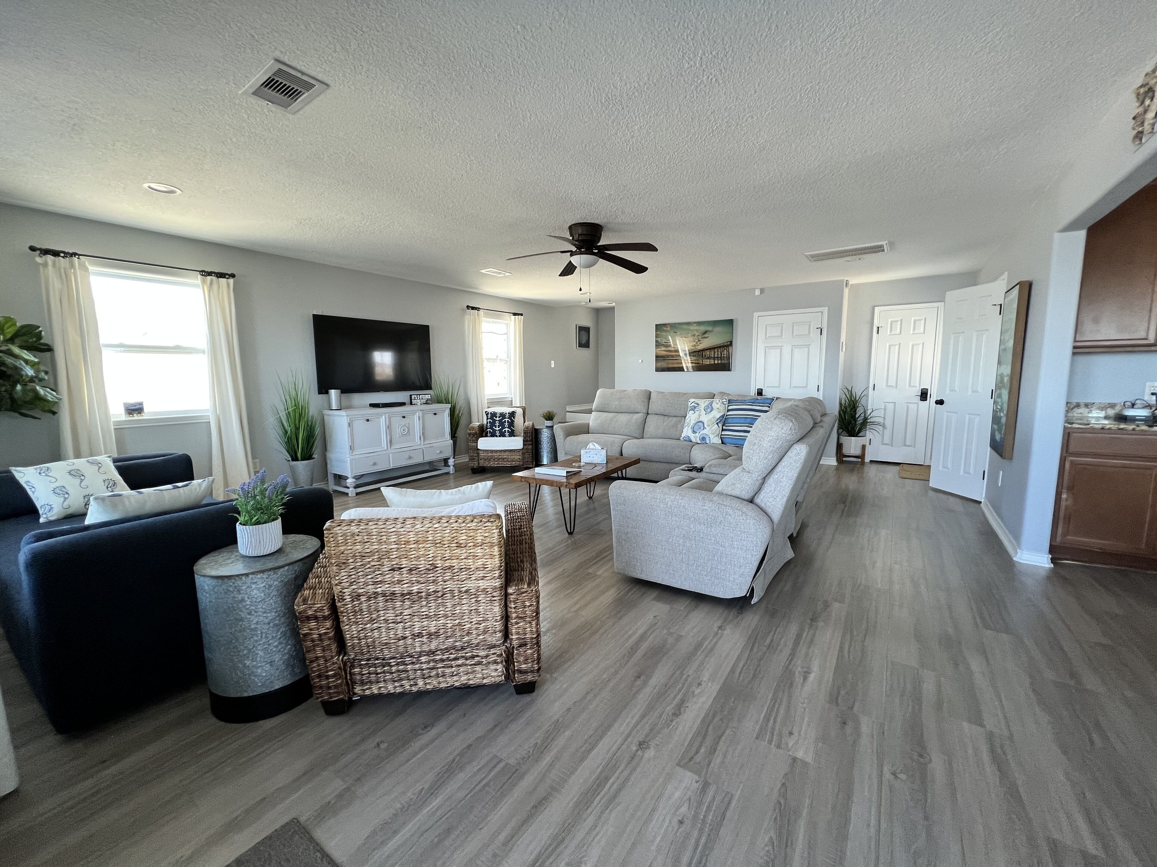 A spacious living room with a grey sectional sofa, a dark blue couch, and a wicker coffee table.