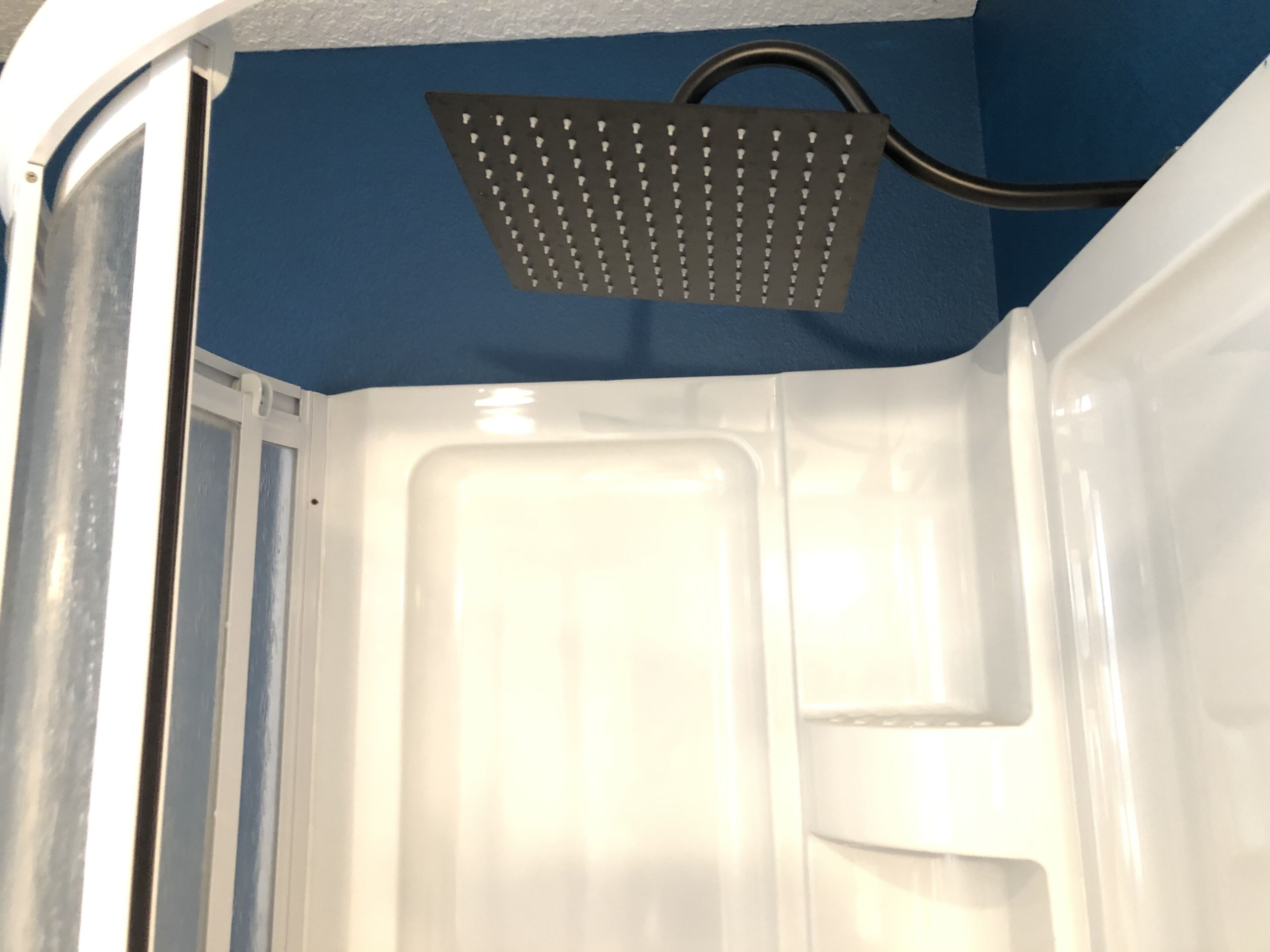 Un baño con ducha empotrada en la pared, una bañera blanca y pared azul.