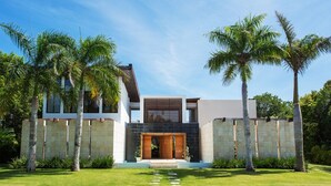 A modern house with a stone facade, a wooden entrance, and a well-maintained lawn. - Luxury villa at Puntacana Resort & Club (Punta Cana)